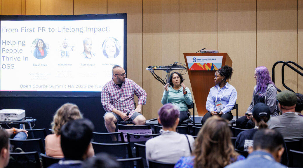 Slide in the background titled From First PR To Lifelong Impact: Helping People Thrive in Open Source with avatars of the 4 speakers who are sitting on tall chairs in front of the slide from left to right Matt Denny, Shuah Khan, Ruth Ikegah, and Dawn Foster. In the foreground are slightly out of focus audience members from the back of the room.