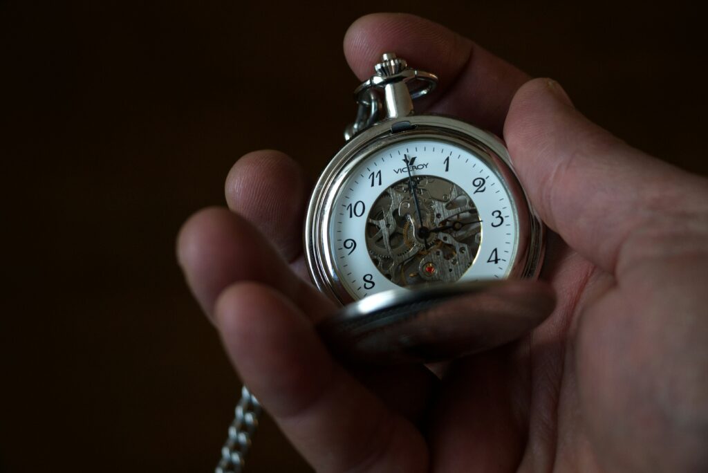 Hand holding an old fashioned, silver pocket watch on a dark background