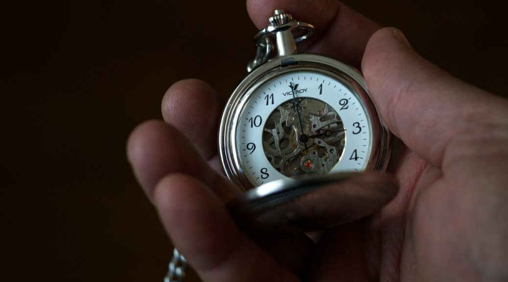 Hand holding an old fashioned, silver pocket watch on a dark background