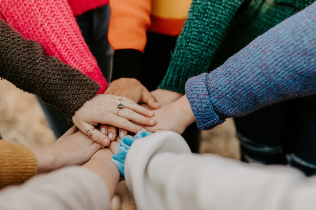 A bunch people's arms with hands in the center with sleeves of various colors..