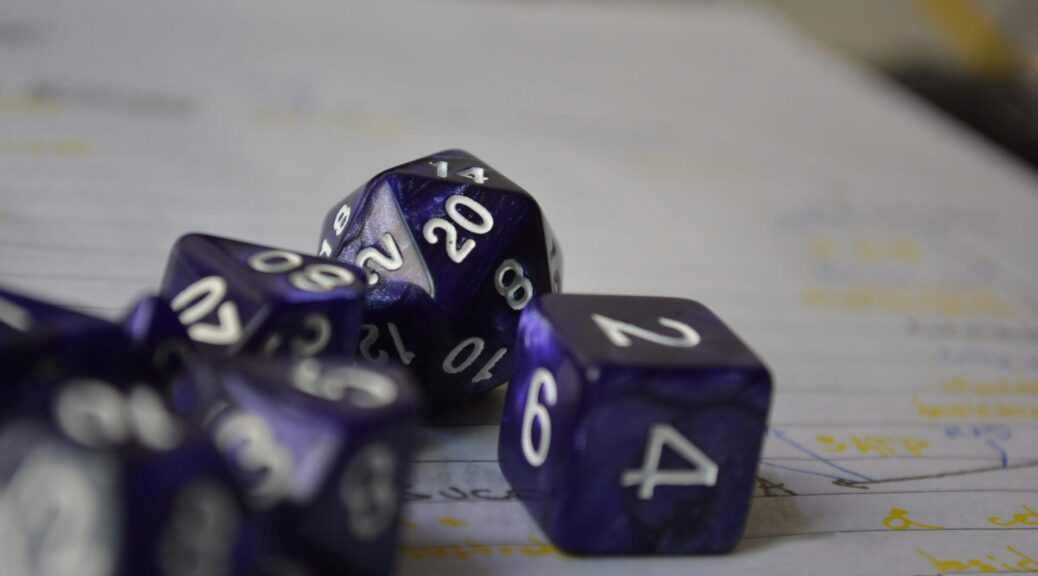 Various types of purple dice with white letters, including a traditional D6 die, a D20, and others. Sitting on a white piece of paper with blurred writing.