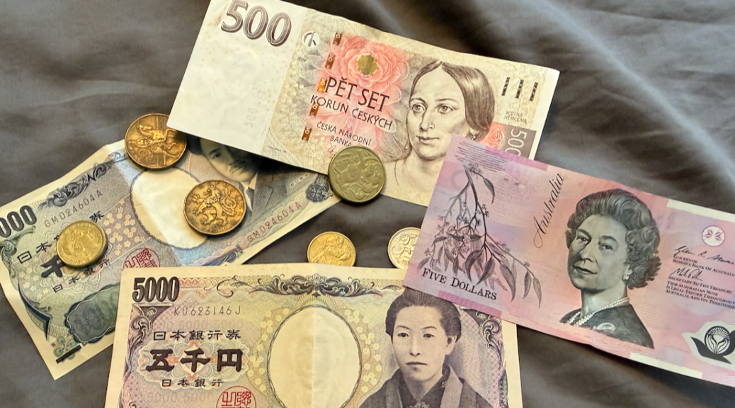 Several old coins and bills from several different countries on a gray cloth background