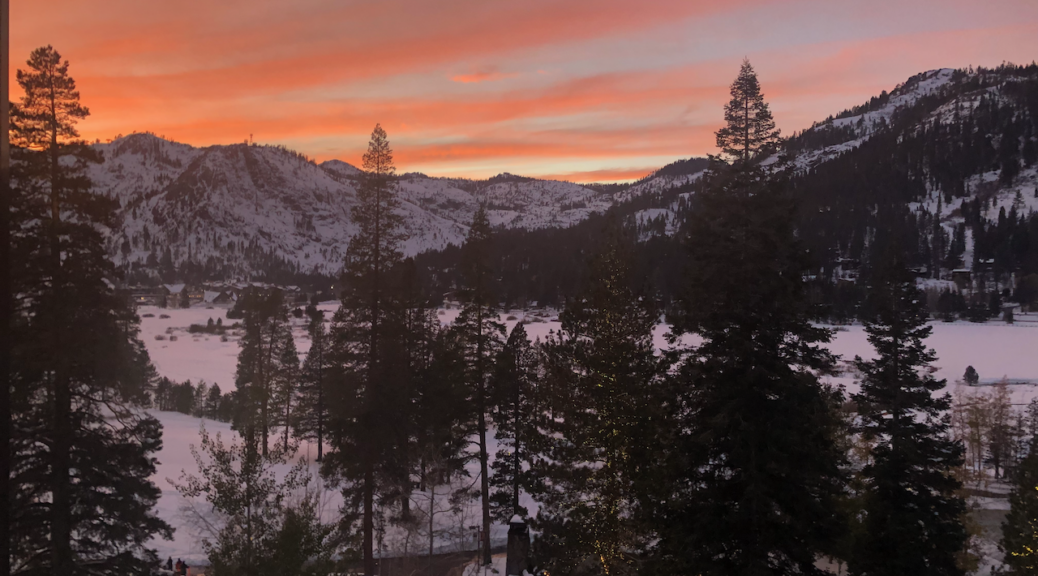 Pink and peach sunset over the mountains with snow on the ground and fir trees in Lake Tahoe